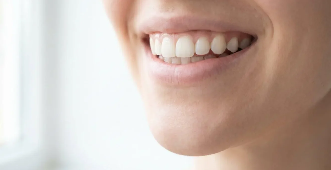 Gros plan d'un sourire naturel et éclatant avec des dents blanches parfaitement alignées, sur fond blanc, symbolisant le résultat de la chirurgie esthétique dentaire moderne